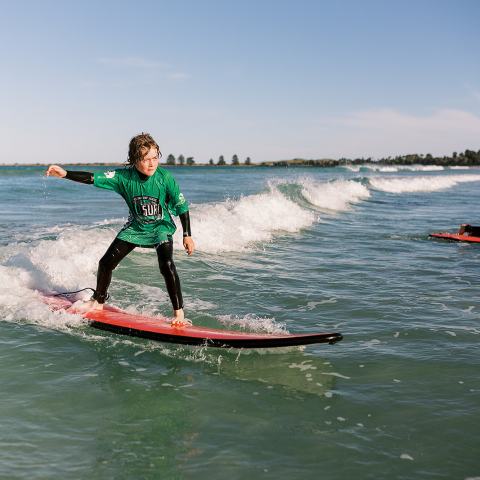 Person surfing on a red surfboard with small waves under a clear blue sky.