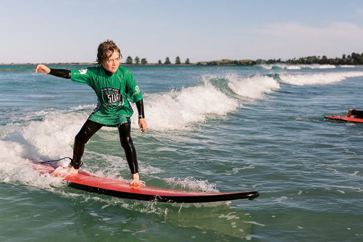 Person surfing on a red surfboard with small waves under a clear blue sky.