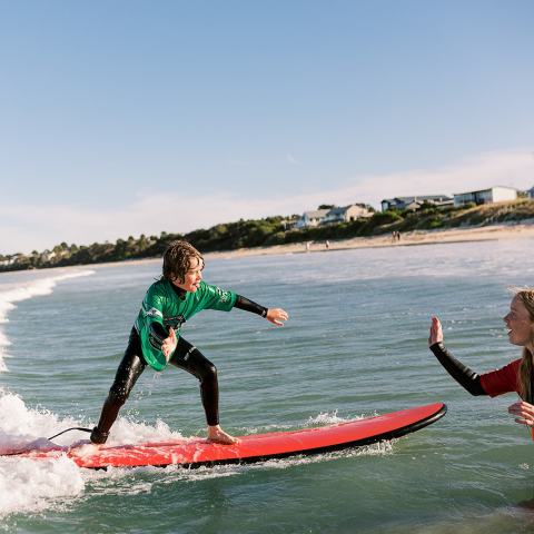 Person surfing on a wave gives a high-five to another in the water.