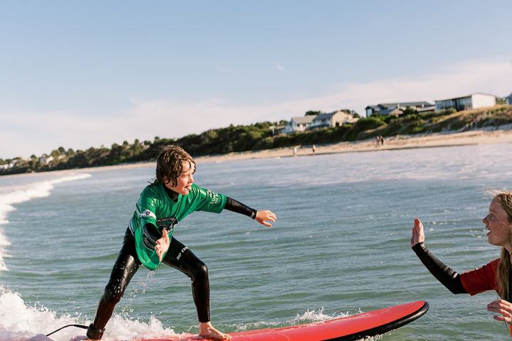 Person surfing on a wave gives a high-five to another in the water.