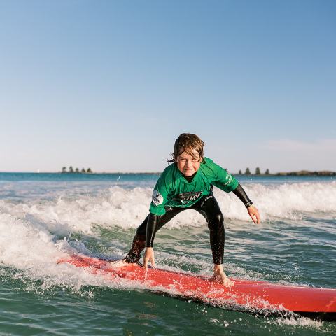 Person surfing on a red surfboard in the ocean, wearing a green shirt with a clear blue sky.