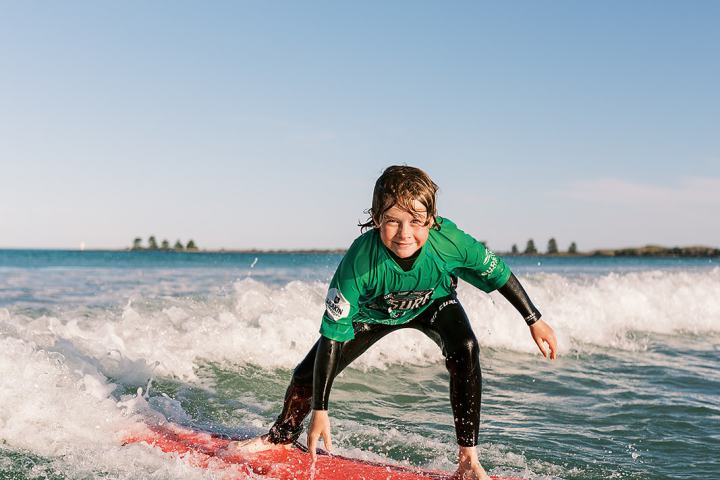Person surfing on a red surfboard in the ocean, wearing a green shirt with a clear blue sky.