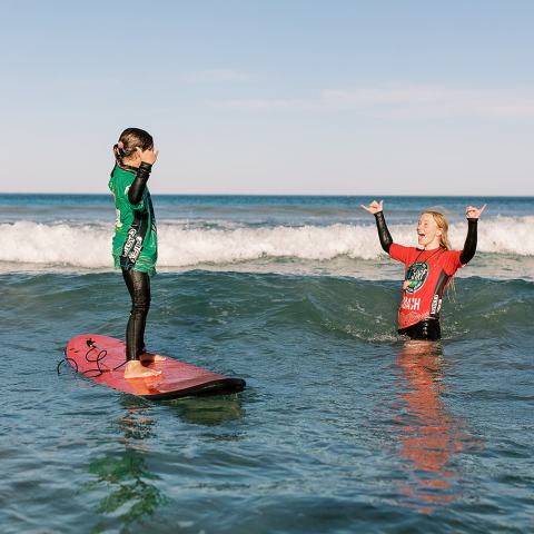 Two people in wetsuits celebrate in ocean near surfboard.