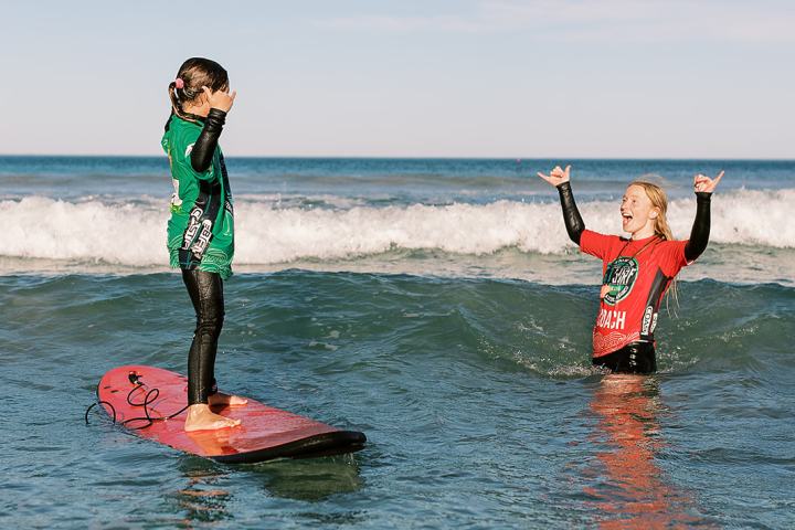 Two people in wetsuits celebrate in ocean near surfboard.