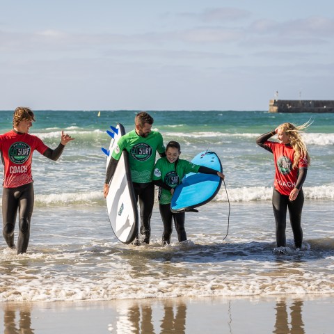 Group of four people in wetsuits with surfboards walking from the ocean.