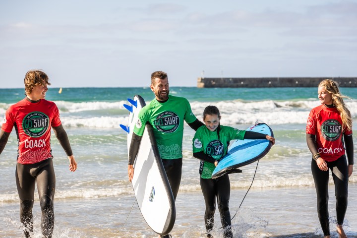 Group of people in wetsuits carrying surfboards by the ocean.